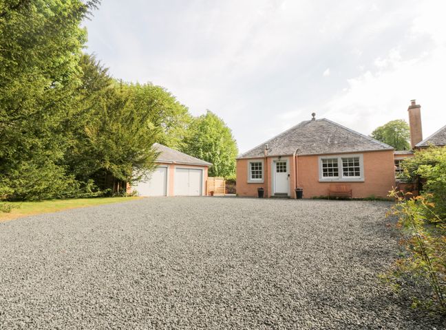 A gravel driveway leading to a house with a double garage and surrounded by trees at Maisies Cottage in Kippenross near Dunblane