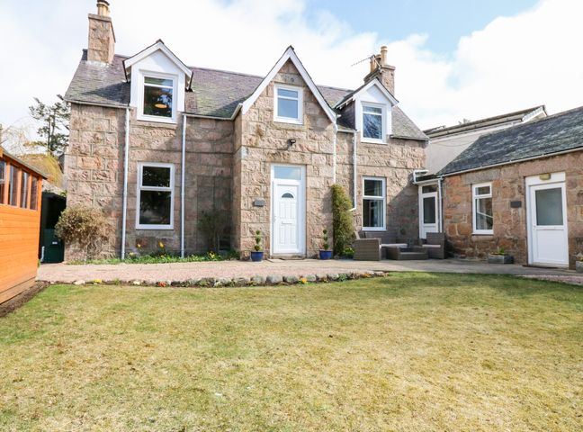 A stone house with white trim and multiple windows with garden and patio furniture at Gairnlea House in Ballater