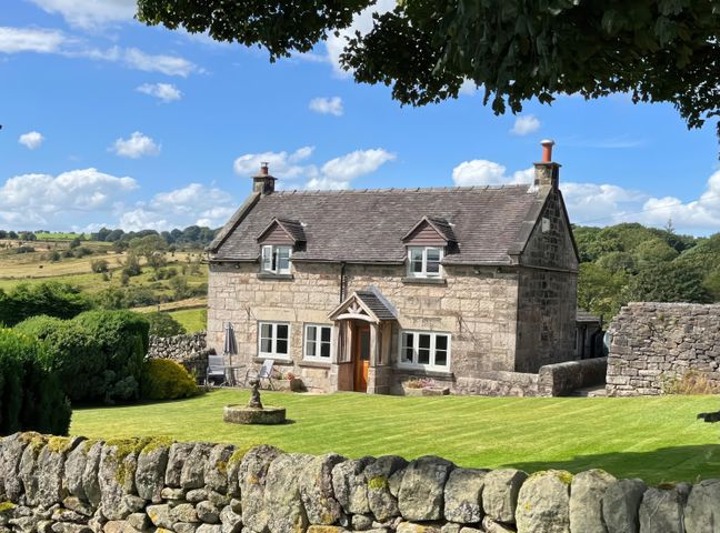 A stone cottage with a lawn and stone wall in a rural area at Sycamore Cottage in Ashbourne