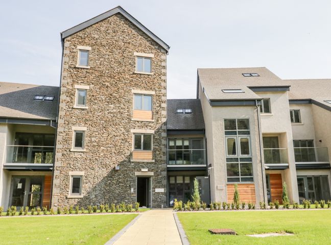 An exterior view of a modern building with stone and stucco walls and balconies at River View in Backbarrow