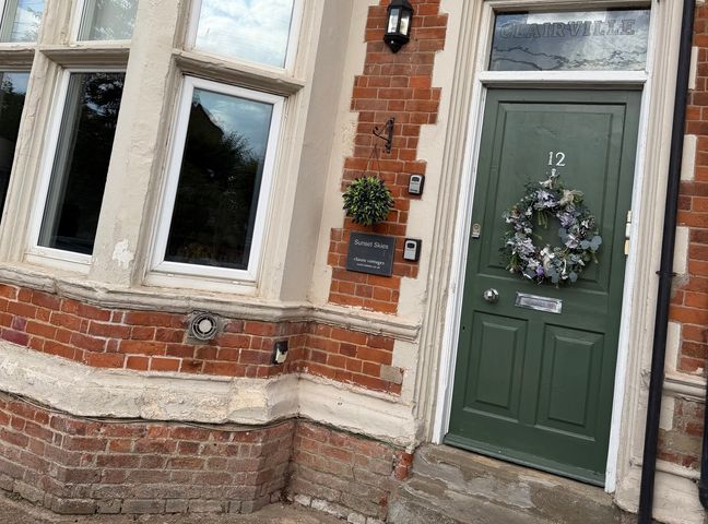 An exterior view of a house entrance with a green door and windows at Clairville, Hunstanton