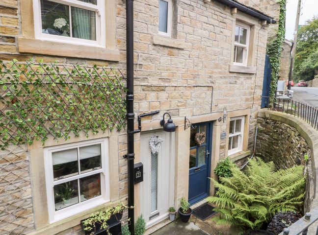 A stone exterior of a house with two doors and three windows and plants in front at 1 Oakleys Holmfirth