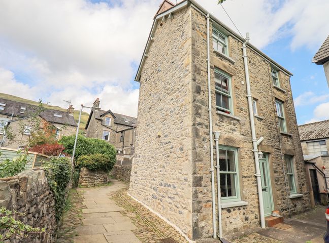Stone house with green window frames and door on a paved street with stone walls at 2 Kings Yard in Sedbergh