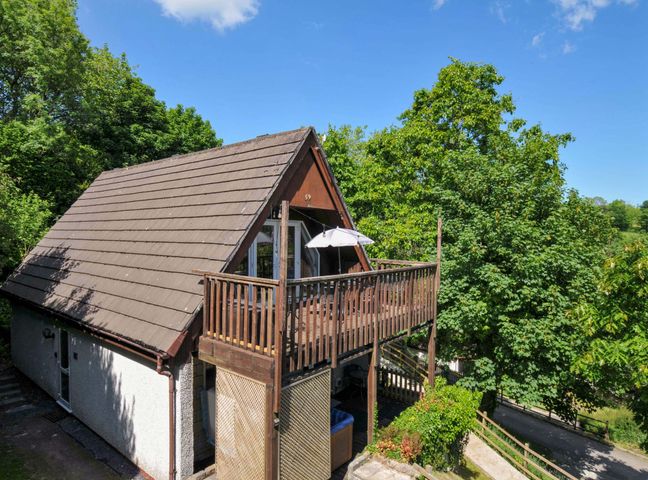 A two-story house with a sloped roof and wooden balcony surrounded by trees at 59 Valley Lodge Callington near Gunnislake