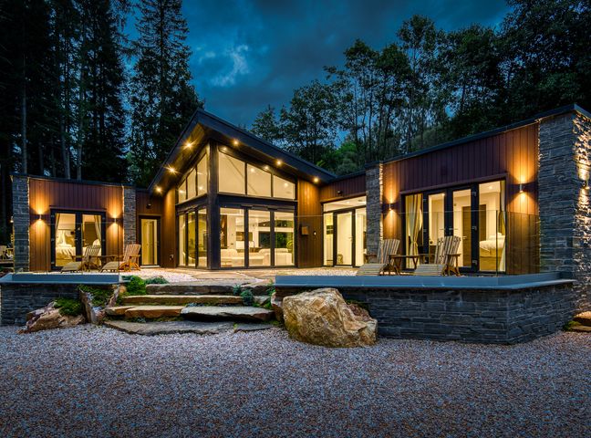 A modern house with large glass windows and outdoor chairs at Heilan Roo in Killiecrankie near Pitlochry and Blair Atholl