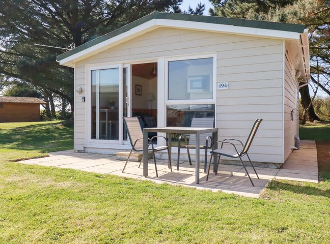 A small house with a patio table and three chairs on a paved area at 194 Atlantic Bays Holiday Park near St Merryn