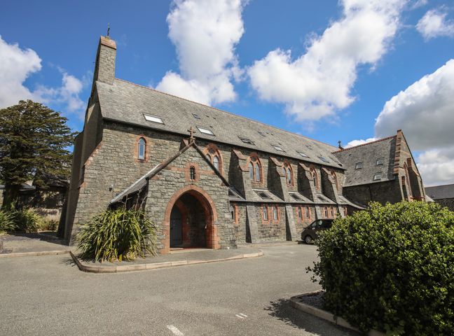 A stone building with arched windows and a slate roof under a blue sky at Dinlle in Criccieth