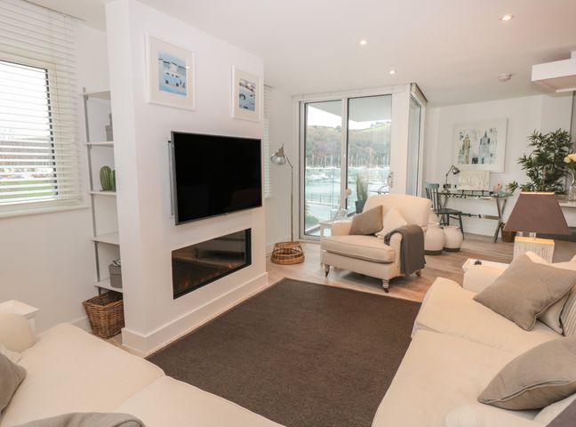 A living room with sofas a wall-mounted TV fireplace and a view of boats through glass doors at 2 Sails in Dartmouth