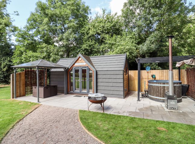 A small outdoor lodge with gray doors and roof beside a hot tub and a canopy structure at Willow Lodge At Bridge Lake Farm Fishery in Chacombe