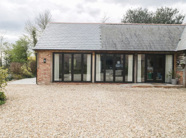 A gravel driveway in front of a building with large windows and a slate roof at The Courtyard - Hilltop Barn in Winterborne Zelston near Wareham