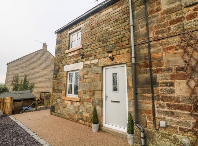 Exterior of a stone house with a white door and two windows with potted plants outside at 1 Town Head in Longnor