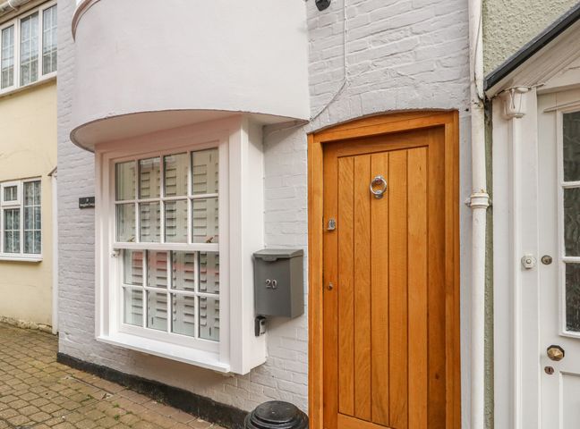 A wooden front door next to a window with shutters and a gray mailbox numbered 20 at Smugglers Cottage in Weymouth