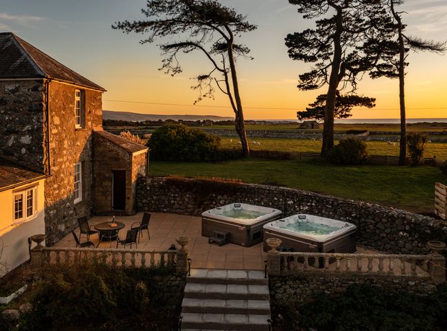 Two hot tubs on a stone patio next to a stone house with a table and chairs at Bennar Fawr in Dyffryn Ardudwy