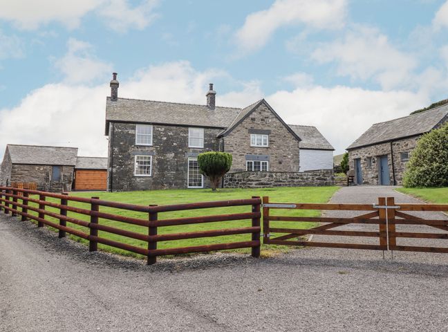A stone farmhouse with wooden gates and a grassy yard at Plas Iolyn in Pentrefoelas near Betws-Y-Coed
