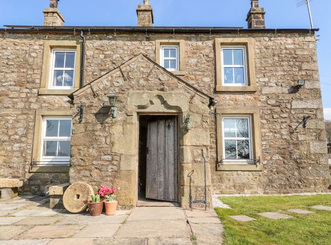 Stone cottage with wooden door flower pots by the entrance and grass in front at Moss Side Retreat in Wigglesworth near Long Preston