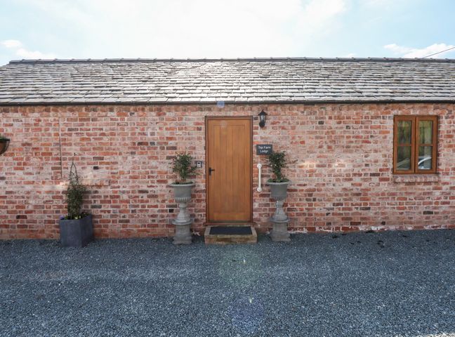 A brick building facade with a wooden door flanked by two planters and a window at Top Farm Lodge in Knockin