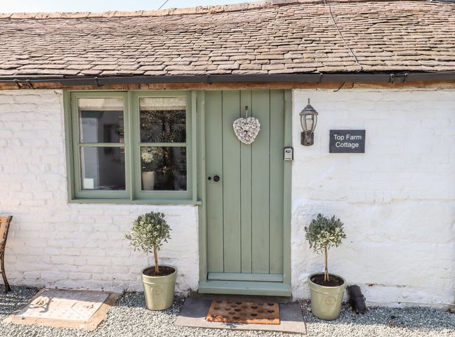 Front door with green paint and heart decoration with two potted plants and a window on a white brick cottage at Top Farm Cottage in Knockin