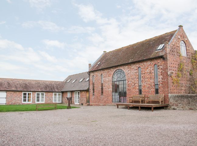 A brick building with large arched windows benches on a wooden deck and a gravel courtyard at Windy Mundy Farm in Pitchford near Shrewsbury