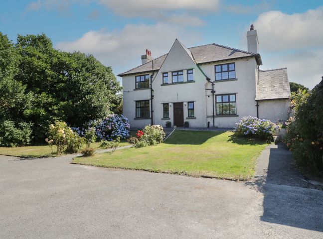 An exterior view of a two-story house with a front lawn and flower bushes at Monarfon in Amlwch