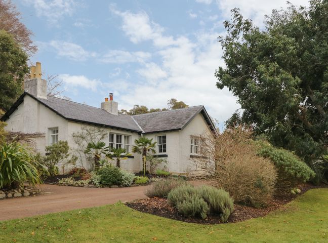 A single story house with white walls surrounded by trees and shrubs at Inverewe - Garden Lodge in Poolewe
