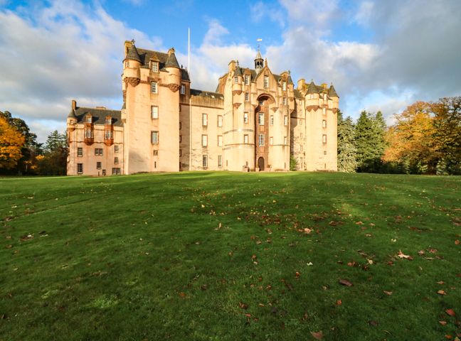 A large castle with turrets and multiple windows on a grassy lawn with trees in the background at The Preston Tower Apartment - Fyvie Castle in Rothienorman