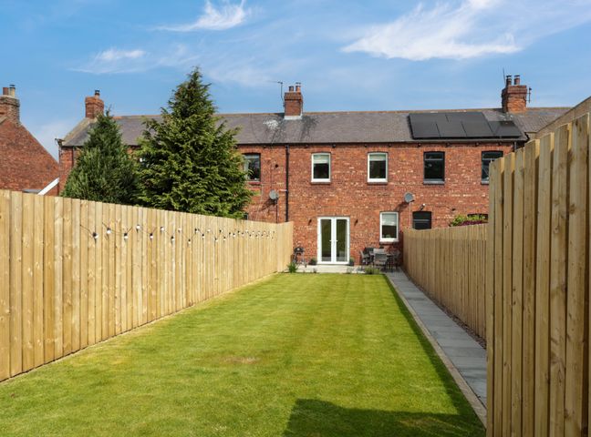 A backyard with grass lawn and wooden fences on each side at The Miners Cottage in Scremerston near Berwick-Upon-Tweed