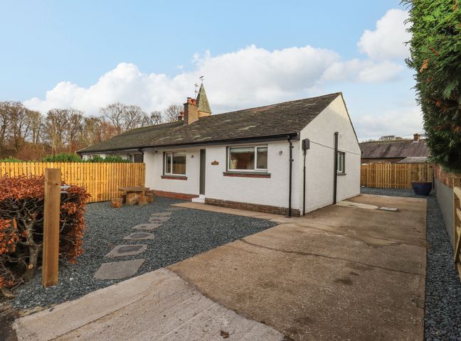 A single-story house with white walls and a gray roof with a paved driveway and a fenced yard at Woodview in Pooley Bridge