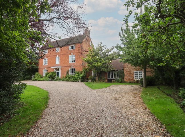 A gravel driveway leading to a large brick house surrounded by trees and grass at The Coach House Apartment in Bredon