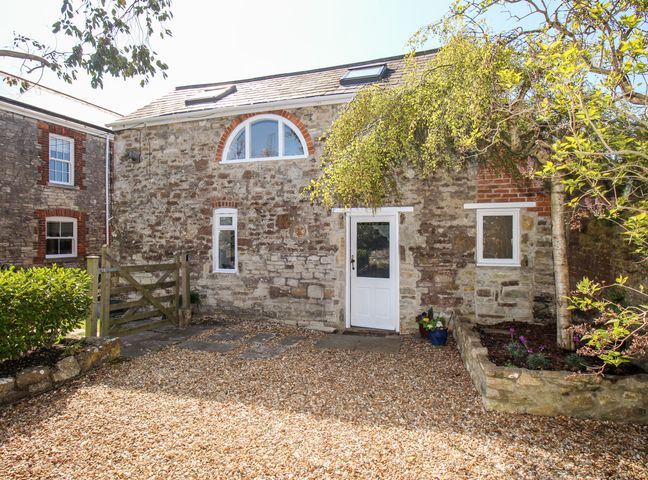 A stone cottage with a white door and windows a wooden gate and gravel driveway at Little Brook in Nottington near Weymouth