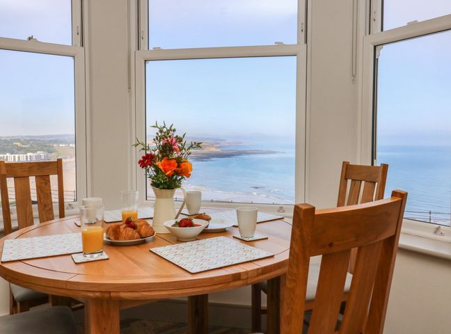 A dining table with breakfast items and flowers by windows overlooking the sea at Apartment 6 in Scarborough