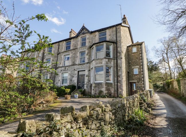 A stone house with multiple windows and a stone wall beside a narrow road at Crows Nest in Arnside