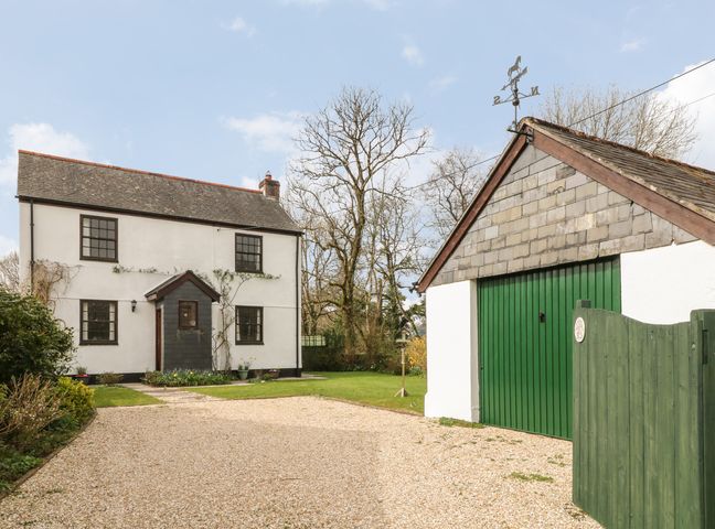 A white two-story house with a gray roof and a green garage door with a green gate outside at Thrushel Cottage in Lifton