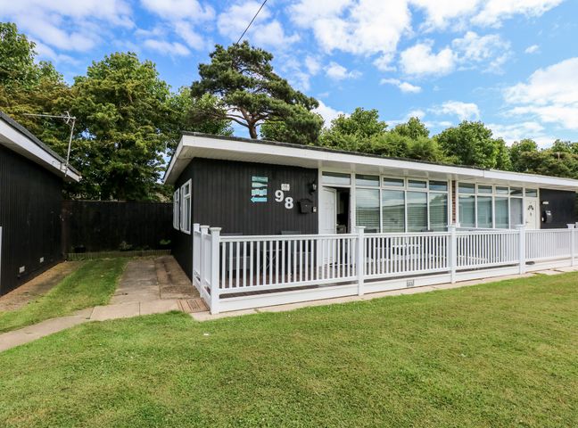 A black house with white railing and a grassy front yard at 98 Cherry Park in Chapel St Leonards
