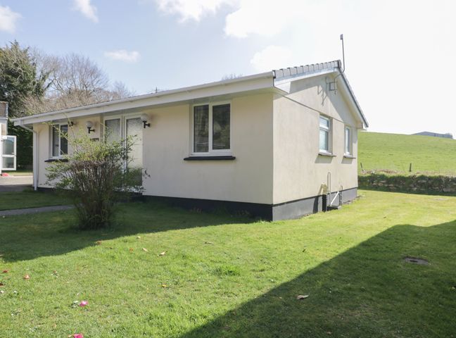 A single story house with a lawn and a bush outside at Watergate Bay in Liskeard