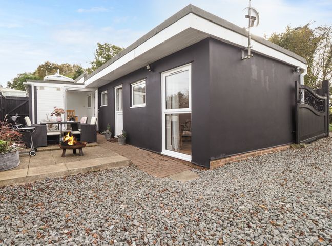 An outdoor patio area with a fire pit seating dining table and chairs next to a black painted single story building with gravel ground at Sleepy Hollow in Ewell Minnis near Dover