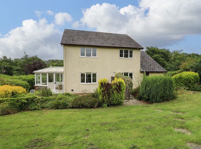A two story house with a conservatory and surrounding garden with bushes and grass at Rhydygroes in Felinfach