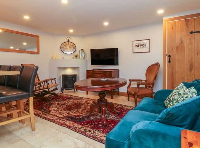 A living room with a round wooden table blue sofa wooden chairs and a wall mounted tv at Proffitts Cottage in Dulverton