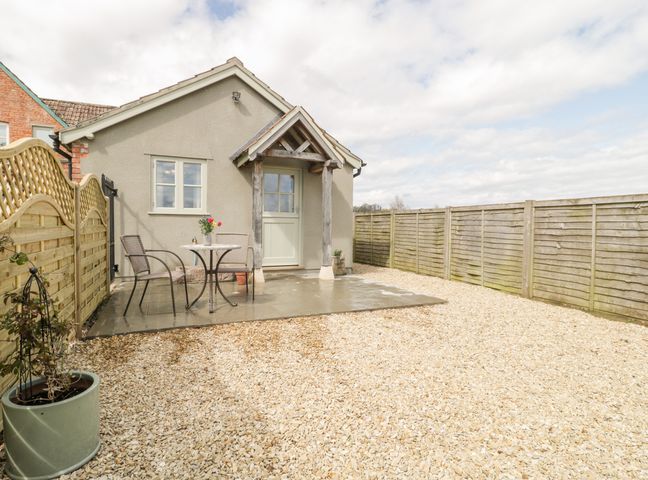A small patio area with a table and two chairs in front of a single-story building with a wooden door and window at The Coal House at Mendip View in Wedmore
