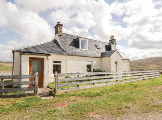 A white cottage with a pitched roof and wooden door surrounded by a wooden fence in a rural area at Loubcroy Farm House in Lairg