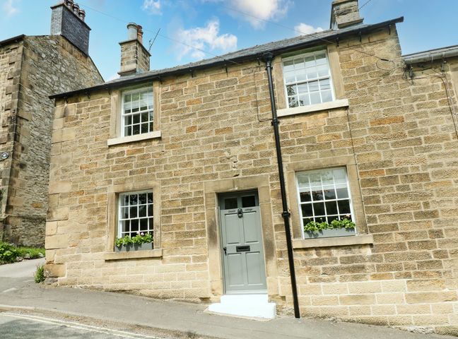 Stone exterior of a two story house with windows and a grey door labeled church cottage in Bakewell