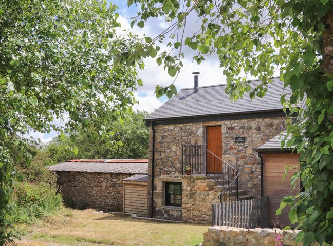 Exterior view of a stone house with stairs leading to a door and trees surrounding the property at The Hayloft in Helston