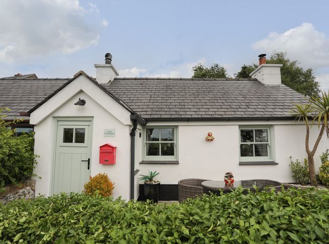 Exterior view of a white cottage with two windows a green door and a red mailbox surrounded by bushes at Cosy Cottage in Llandegfan near Menai Bridge