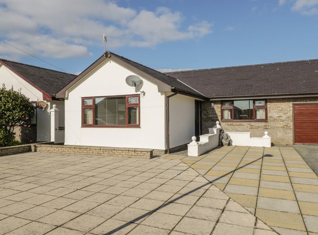 A paved driveway and front yard with a white building and a garage at Rhos Deiniol in Morfa Bychan