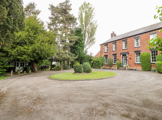 A front view of a brick house with a circular driveway and trimmed bushes at Ley Fields Farm in Cheadle
