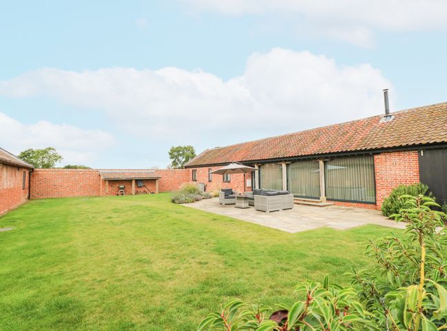 A garden with a tiled patio and outdoor seating in front of a red brick building at Shorthorn Barn in Attlebridge near Taverham