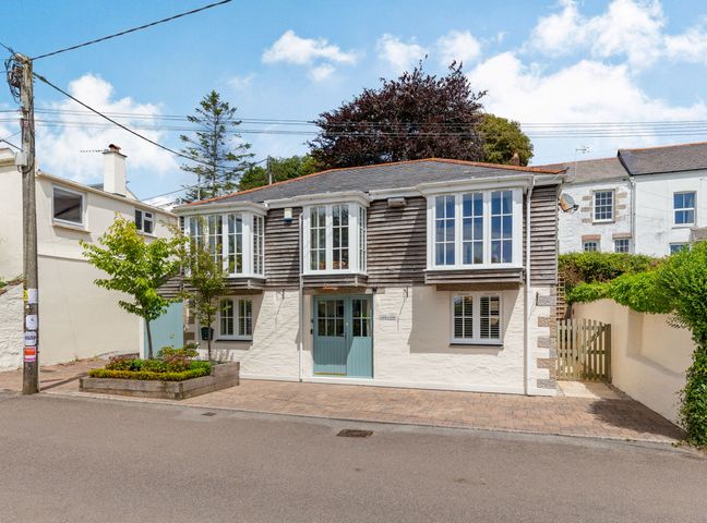A two story house with bay windows and a green door next to a raised flower bed on a paved street at Armando in Devoran Cornwall