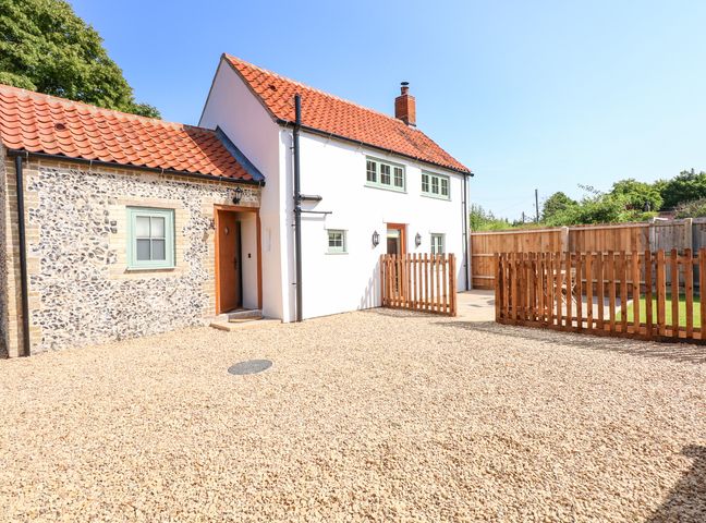 A cottage with tiled roof gravel driveway wooden fences and green lawn at Postbox Cottage in Feltwell