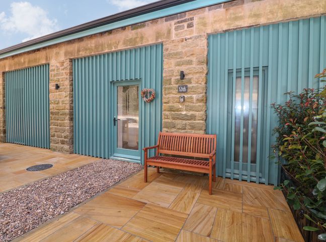 An exterior view of a stone and blue corrugated metal wall with a door, wooden bench, and gravel path at Oak Cottage in Bolsterstone Ewden Village