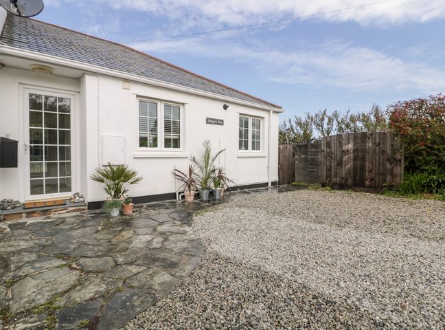 The exterior of a white house with a stone and gravel driveway and potted plants near the entrance at Badgers Way in Tintagel