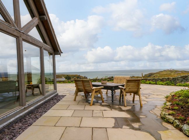 An outdoor patio with wooden chairs and a table overlooking the sea at Balog Farm in Amlwch